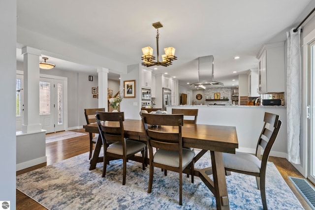 9086 N Tottenham Dr, Traverse City, MI 49685 - dining space featuring an inviting chandelier, decorative columns, dark wood-type flooring, and visible vents