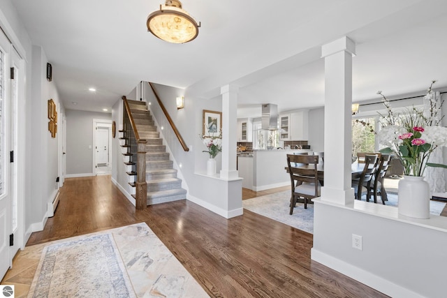 9086 N Tottenham Dr, Traverse City, MI 49685 - foyer featuring decorative columns, baseboard heating, wood finished floors, baseboards, and stairs