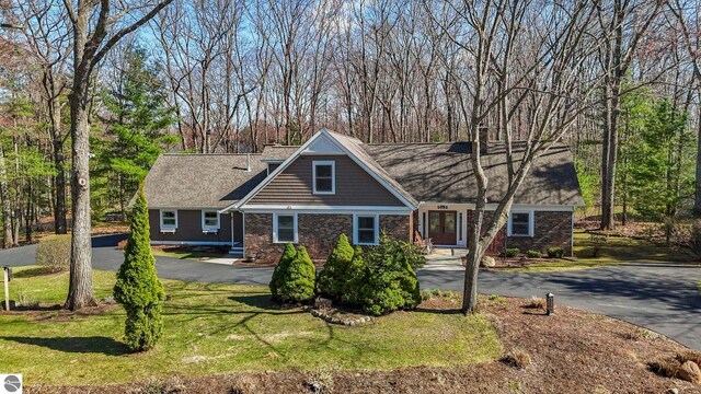 9086 N Tottenham Dr, Traverse City, MI 49685 - view of front facade with a chimney, a front yard, brick siding, and aphalt driveway