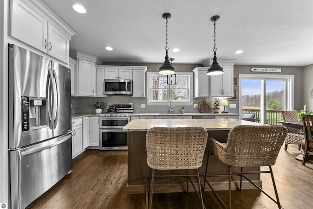 kitchen featuring decorative backsplash, appliances with stainless steel finishes, a center island, a sink, and dark wood-type flooring
