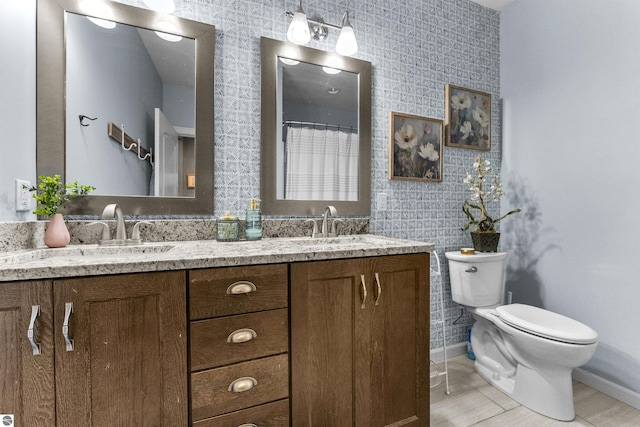 full bath featuring baseboards, a sink, double vanity, and toilet