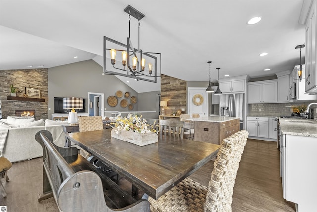 dining space featuring a stone fireplace, lofted ceiling, a chandelier, and dark wood-style floors