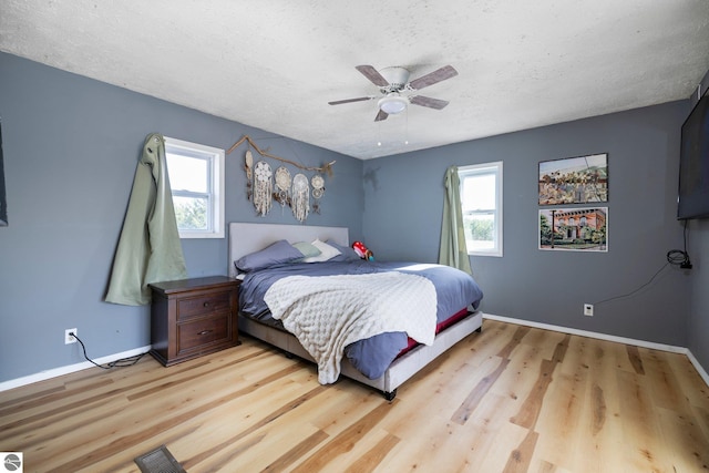 bedroom with a ceiling fan, a textured ceiling, visible vents, light wood-type flooring, and baseboards