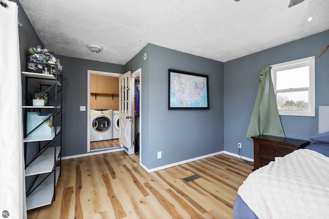 bedroom featuring light wood-type flooring, baseboards, a textured ceiling, and washing machine and dryer