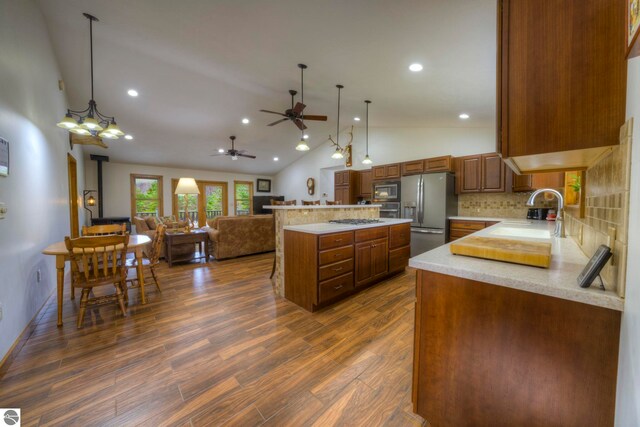 kitchen featuring backsplash, appliances with stainless steel finishes, vaulted ceiling, a sink, and ceiling fan with notable chandelier