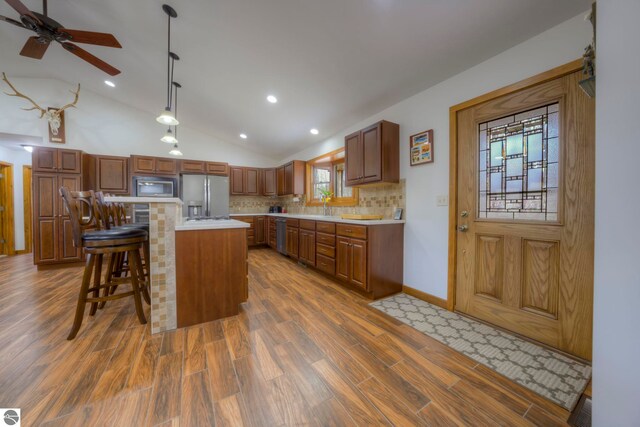 kitchen with dark wood-style flooring, light countertops, tasteful backsplash, appliances with stainless steel finishes, and vaulted ceiling