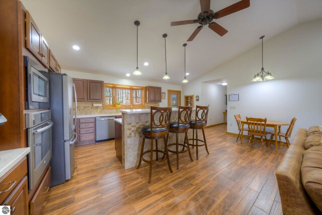 kitchen featuring a breakfast bar area, appliances with stainless steel finishes, brown cabinetry, and light countertops