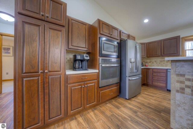 kitchen featuring appliances with stainless steel finishes, light countertops, decorative backsplash, wood finished floors, and lofted ceiling