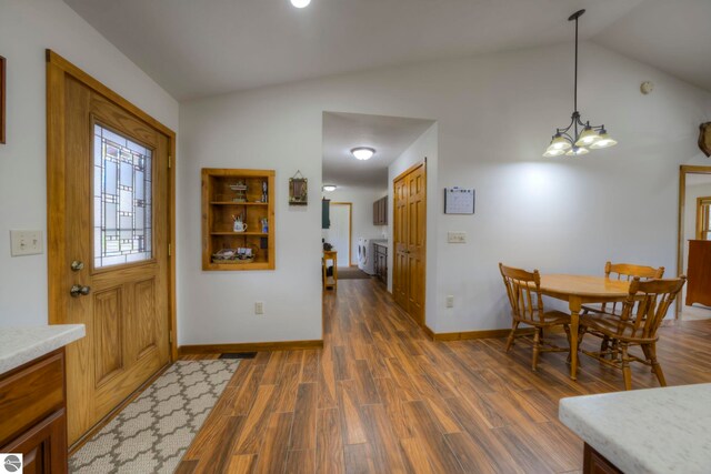 dining room featuring dark wood-style flooring, separate washer and dryer, a chandelier, baseboards, and vaulted ceiling