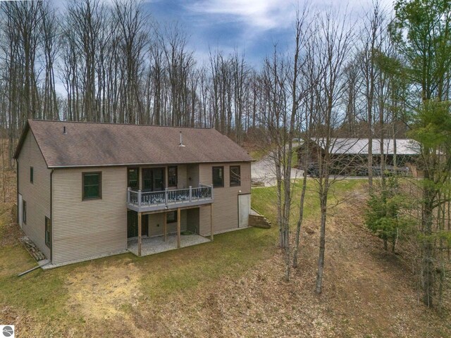 rear view of property with a lawn, a shingled roof, a patio area, and a wooden deck