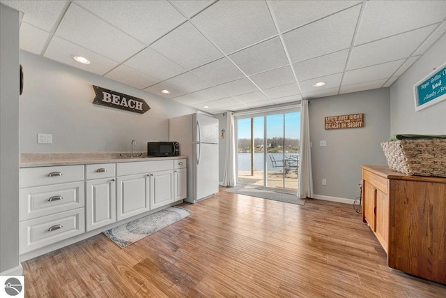 bar with freestanding refrigerator, black microwave, a paneled ceiling, and light wood finished floors