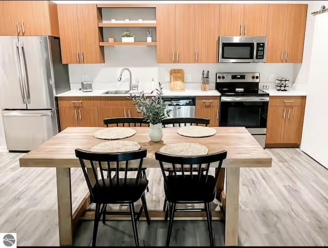 kitchen featuring light countertops, stainless steel appliances, brown cabinetry, and a sink