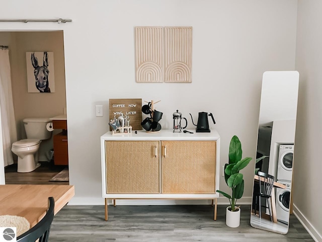 bar featuring baseboards, wood finished floors, and stacked washer and clothes dryer