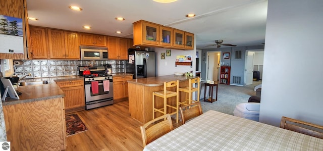 kitchen featuring ceiling fan, a kitchen breakfast bar, brown cabinetry, stainless steel appliances, and tasteful backsplash