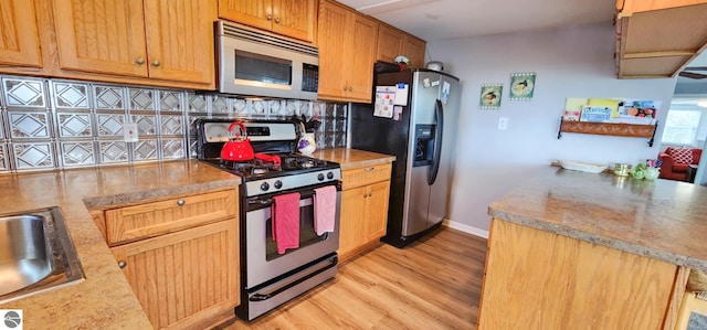 kitchen featuring a sink, light wood-style flooring, stainless steel appliances, baseboards, and decorative backsplash