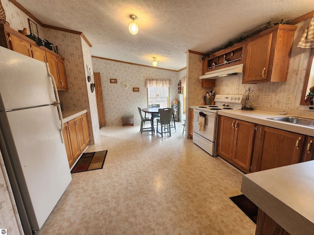 kitchen with white appliances, brown cabinetry, wallpapered walls, under cabinet range hood, and ornamental molding