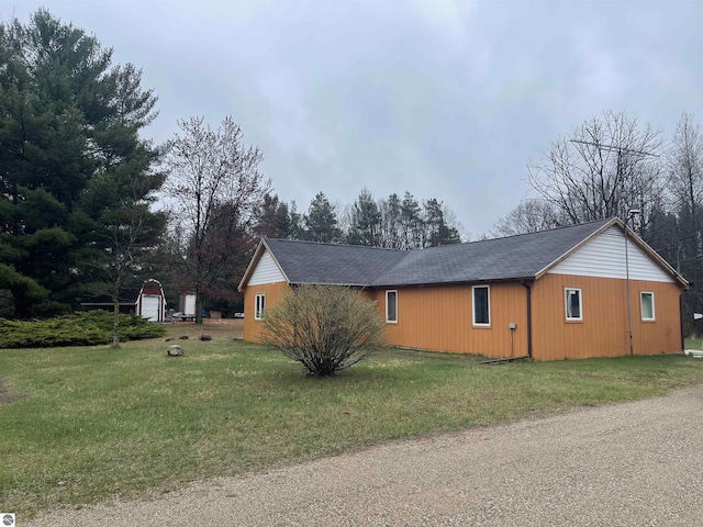 view of property exterior with a yard, an outdoor structure, and roof with shingles