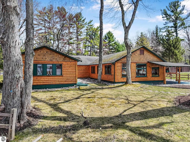 rear view of house with a lawn, log veneer siding, fence, and roof with shingles
