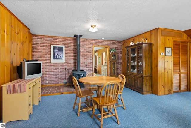 carpeted dining area with wooden walls, a textured ceiling, brick wall, and a wood stove