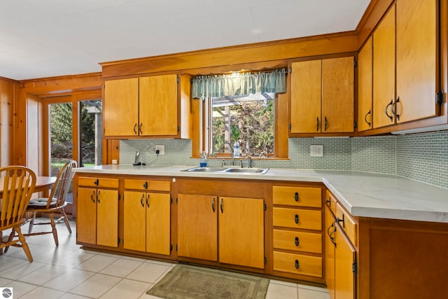 kitchen featuring a sink, light countertops, brown cabinetry, light tile patterned floors, and tasteful backsplash