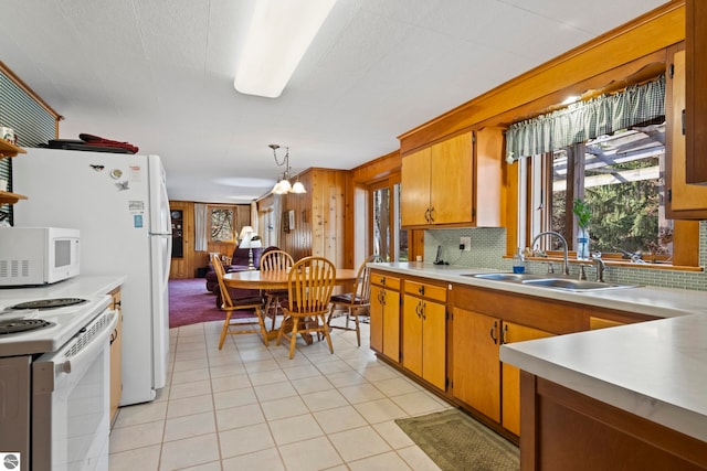 kitchen with wood walls, white appliances, light countertops, brown cabinets, and a sink