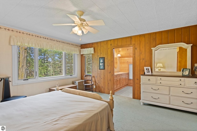 bedroom with ensuite bathroom, a ceiling fan, carpet flooring, and wood walls