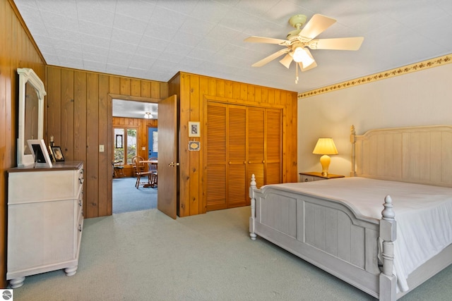 bedroom featuring a closet, carpet flooring, a ceiling fan, and wooden walls