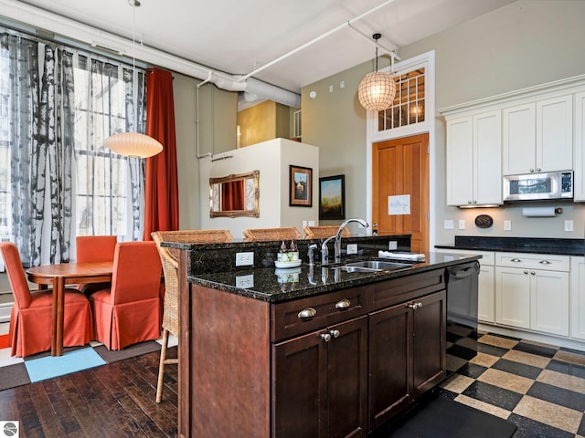 kitchen with a towering ceiling, a kitchen island with sink, a breakfast bar, stainless steel microwave, and a sink