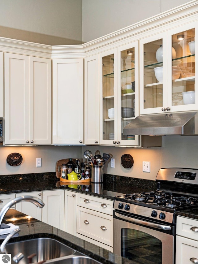 kitchen featuring white cabinets, appliances with stainless steel finishes, a sink, dark stone countertops, and under cabinet range hood