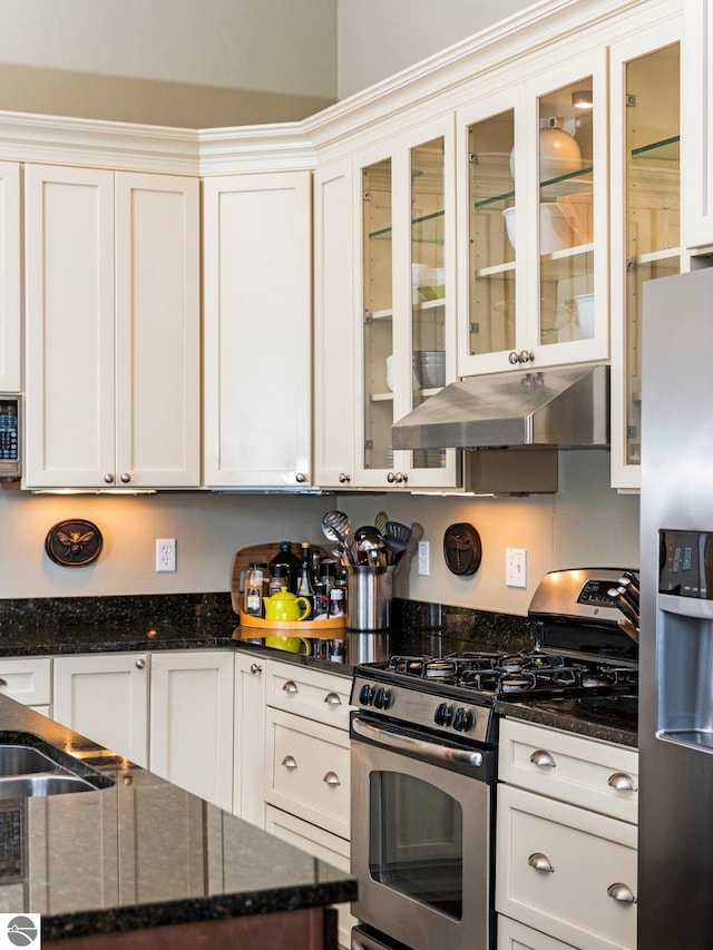 kitchen featuring under cabinet range hood, appliances with stainless steel finishes, glass insert cabinets, and dark stone counters