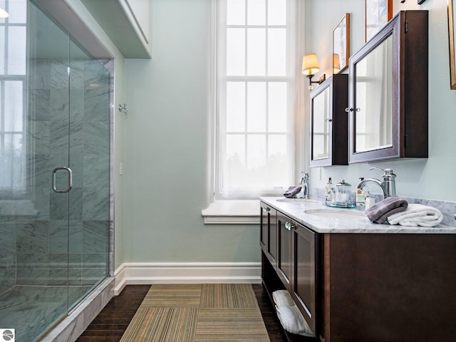 full bath featuring double vanity, baseboards, a shower stall, and a sink