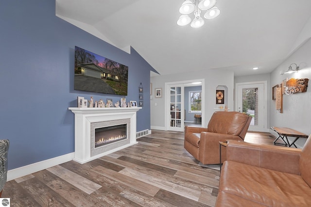 living room with a notable chandelier, visible vents, wood finished floors, lofted ceiling, and a lit fireplace