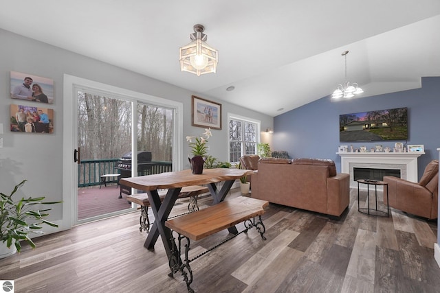 dining area with an inviting chandelier, wood finished floors, vaulted ceiling, and a fireplace