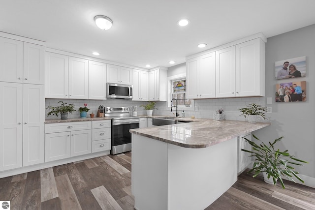 kitchen featuring a peninsula, white cabinets, appliances with stainless steel finishes, and dark wood-style floors