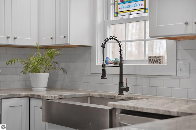 kitchen with backsplash, white cabinetry, light stone countertops, and a sink