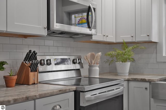 kitchen with appliances with stainless steel finishes, tasteful backsplash, light stone countertops, and white cabinets