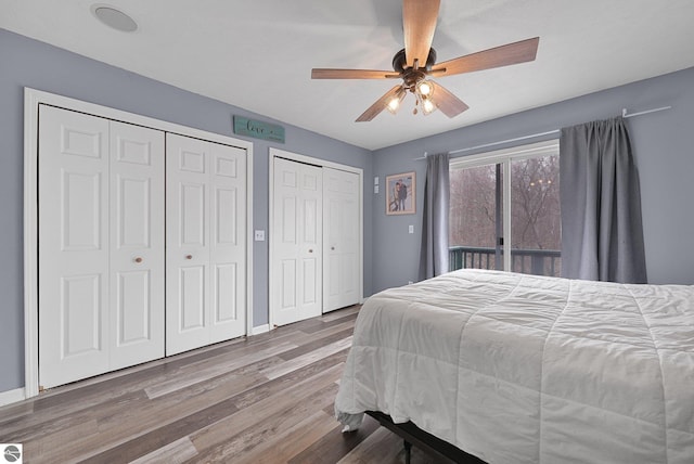 bedroom featuring access to outside, ceiling fan, two closets, baseboards, and wood finished floors