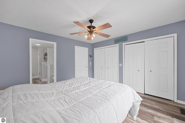 bedroom featuring visible vents, wood finished floors, two closets, baseboards, and ceiling fan