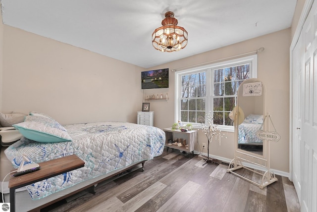 bedroom with baseboards, a notable chandelier, wood finished floors, and a closet
