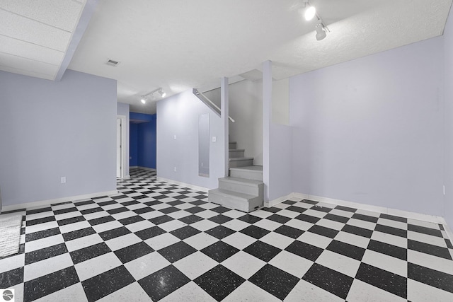 finished below grade area with visible vents, stairway, track lighting, baseboards, and tile patterned floors