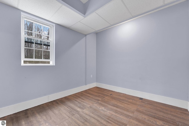 empty room featuring baseboards, a drop ceiling, and wood finished floors