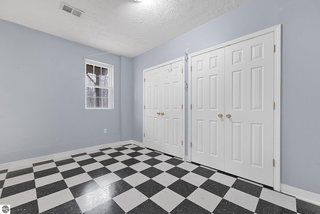 unfurnished bedroom featuring visible vents, multiple closets, baseboards, a textured ceiling, and tile patterned floors