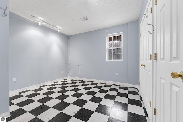 empty room featuring baseboards, rail lighting, a textured ceiling, and tile patterned floors