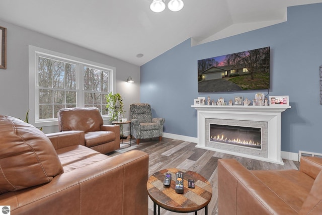 living room with baseboards, vaulted ceiling, a glass covered fireplace, and wood finished floors