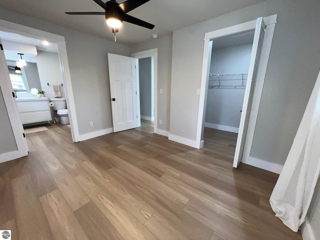 unfurnished bedroom featuring a walk in closet, baseboards, wood finished floors, and ensuite bath