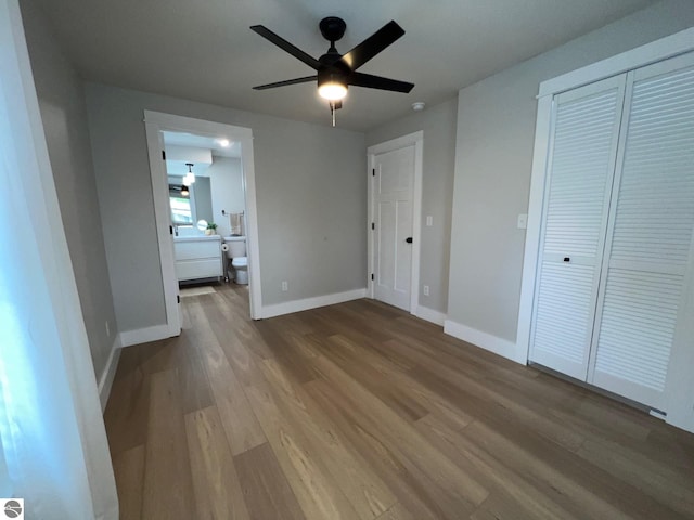 unfurnished bedroom featuring baseboards, a closet, wood finished floors, and connected bathroom