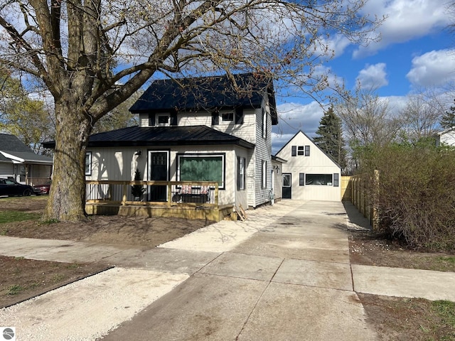 traditional home featuring an outdoor structure, a garage, concrete driveway, covered porch, and metal roof
