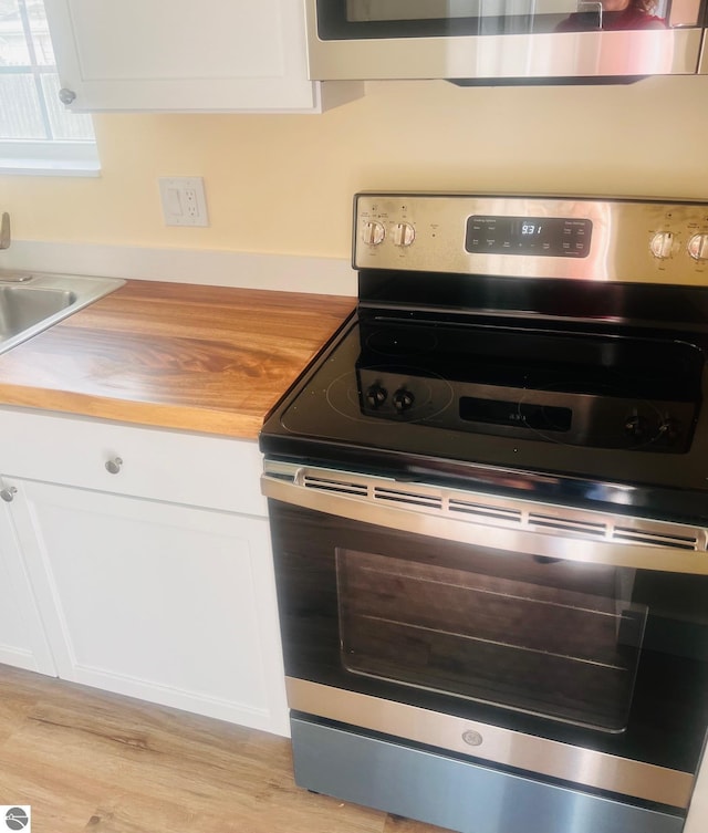 interior details with butcher block countertops, light wood-style flooring, white cabinetry, and stainless steel appliances