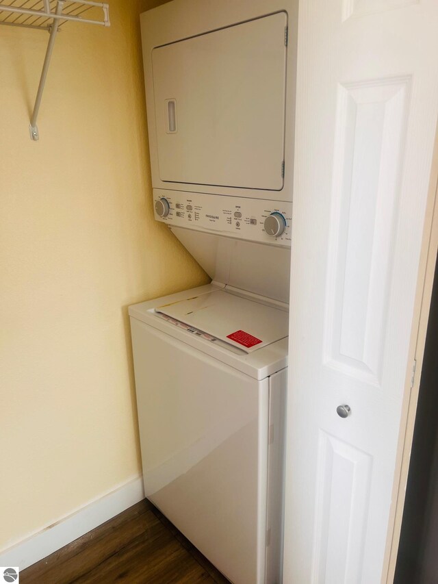 washroom featuring laundry area, baseboards, dark wood-style flooring, and stacked washer / dryer