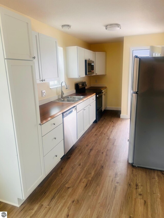 kitchen with baseboards, white cabinets, a sink, dark wood finished floors, and stainless steel appliances